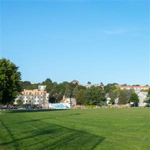 Empty bright green grass field with city scape and blue sky behind it
